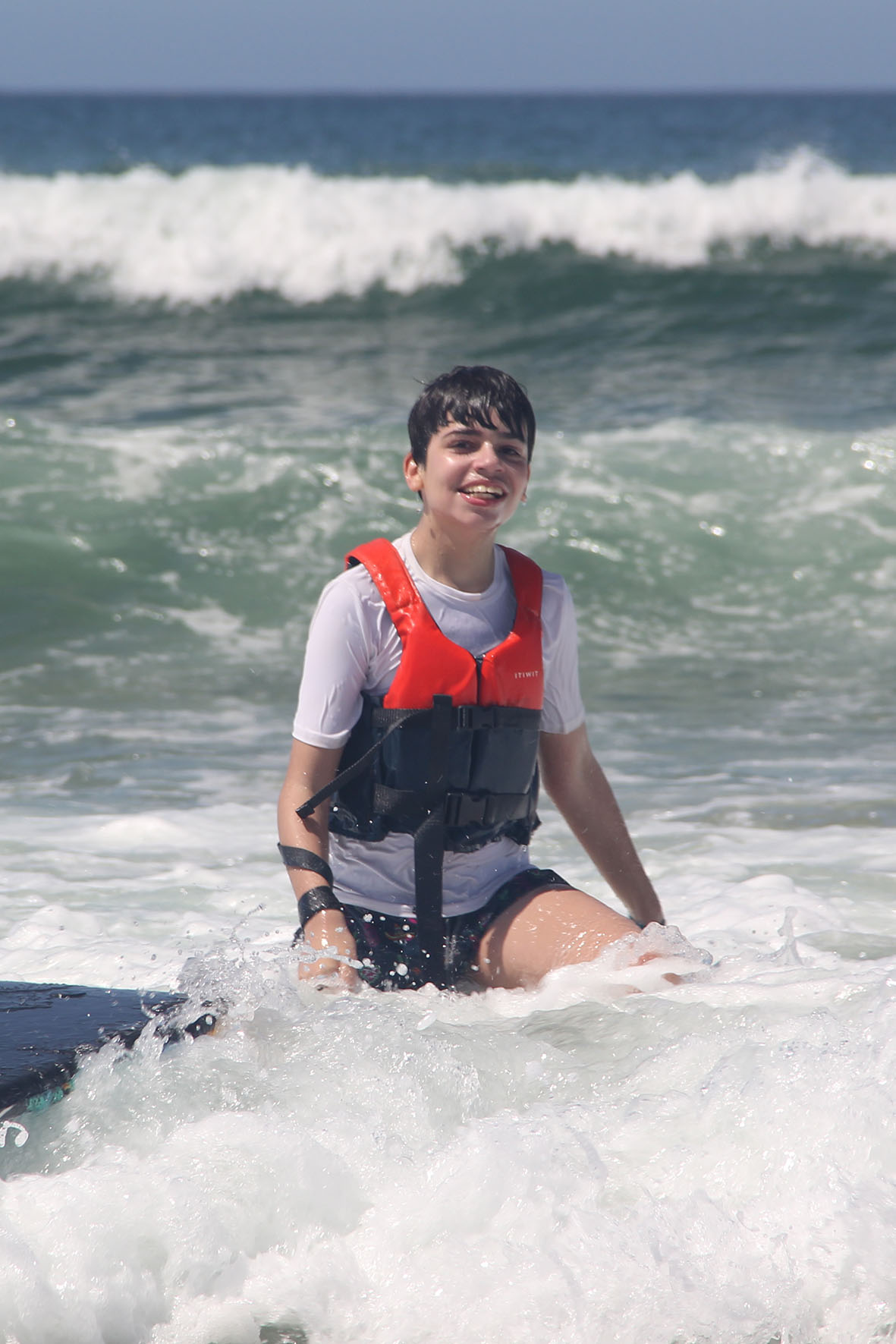 Alexandre, a 14-year-old boy, sitting in the sea water wearing an orange life jacket