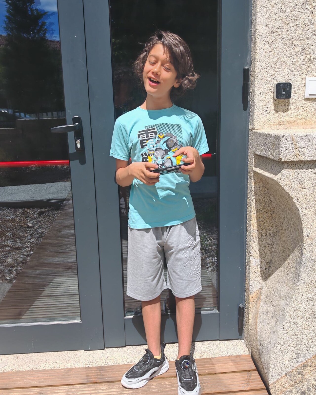 Rafael, a 12-year-old boy in a blue t-shirt, holding a phone at the door of a building