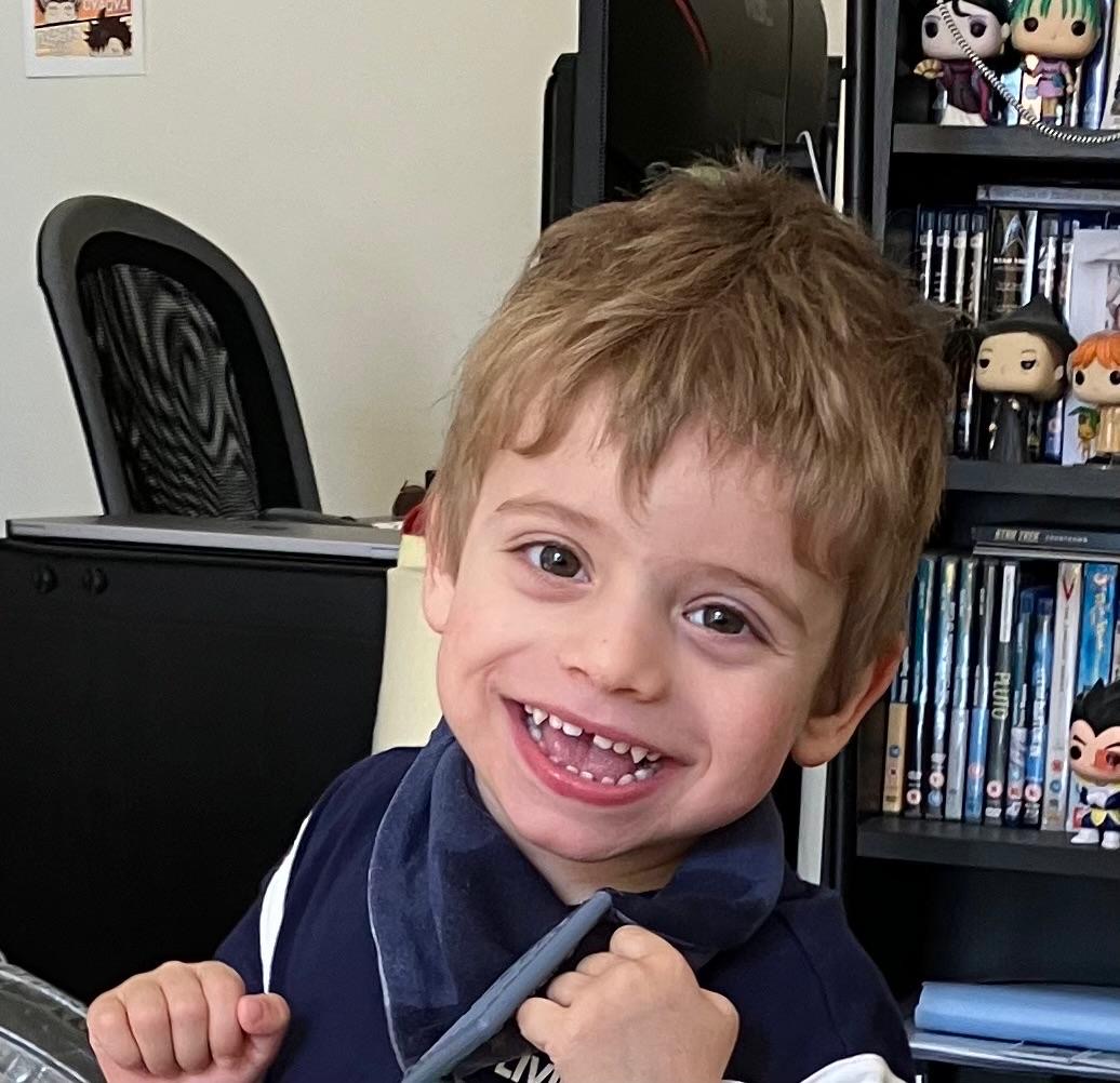 Rafa, a 3-year-old boy, smiling in front of a bookshelf with books and figures